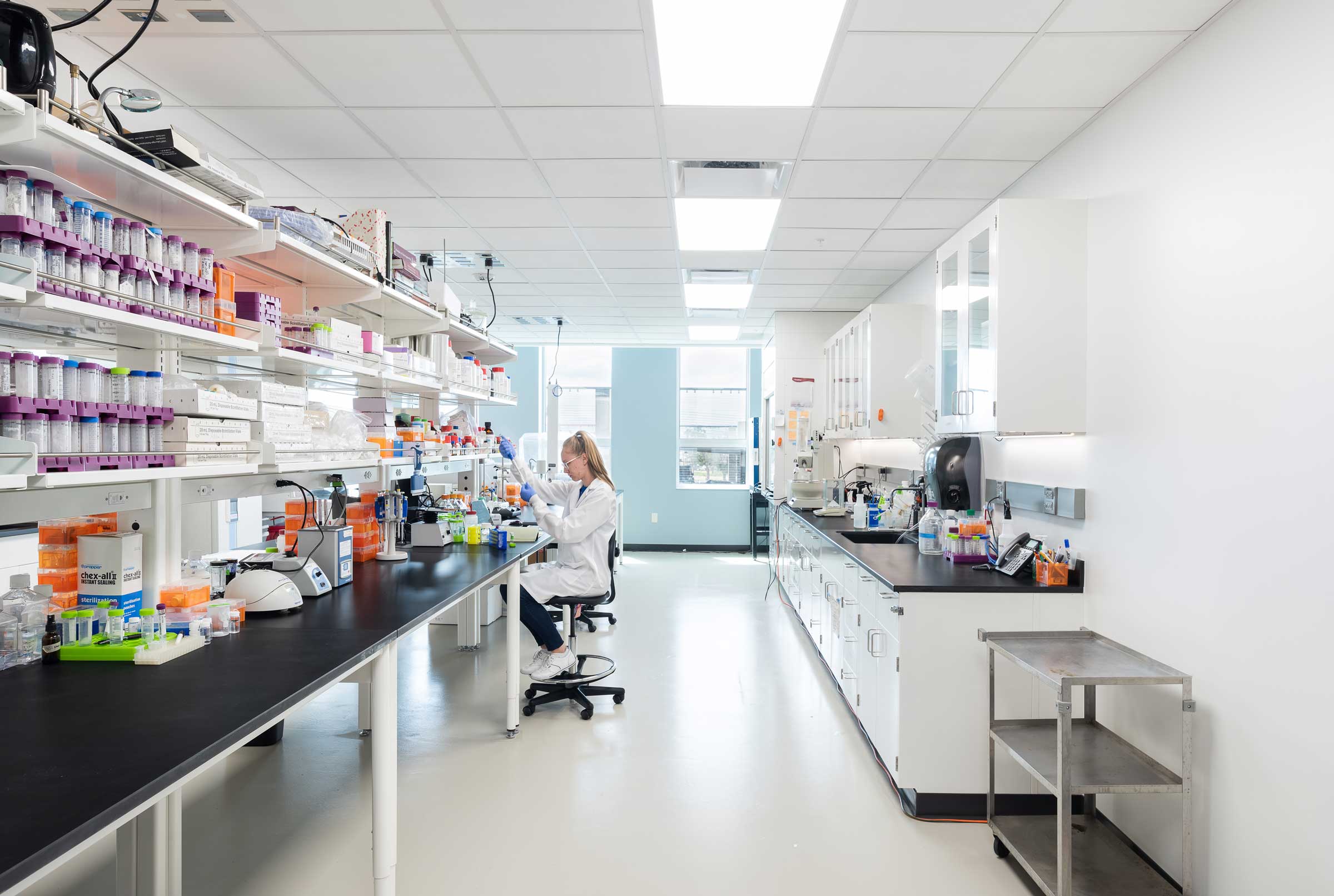 A researcher in a white lab coat examines a sample in a modern bioscience laboratory.