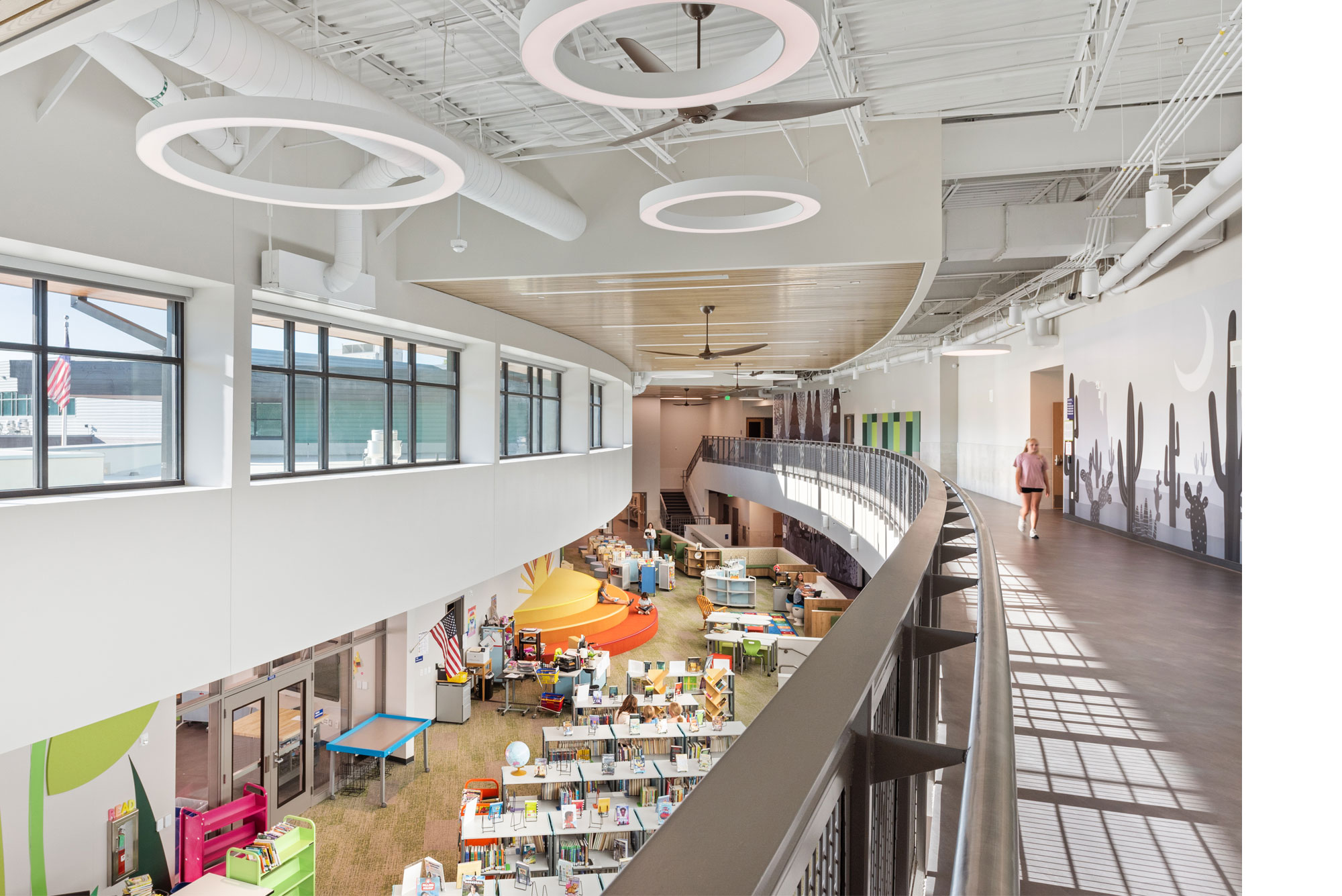Overhead view of Little Raven Elementary School library with a curved walkway, sun-shaped reading area, and colorful murals.