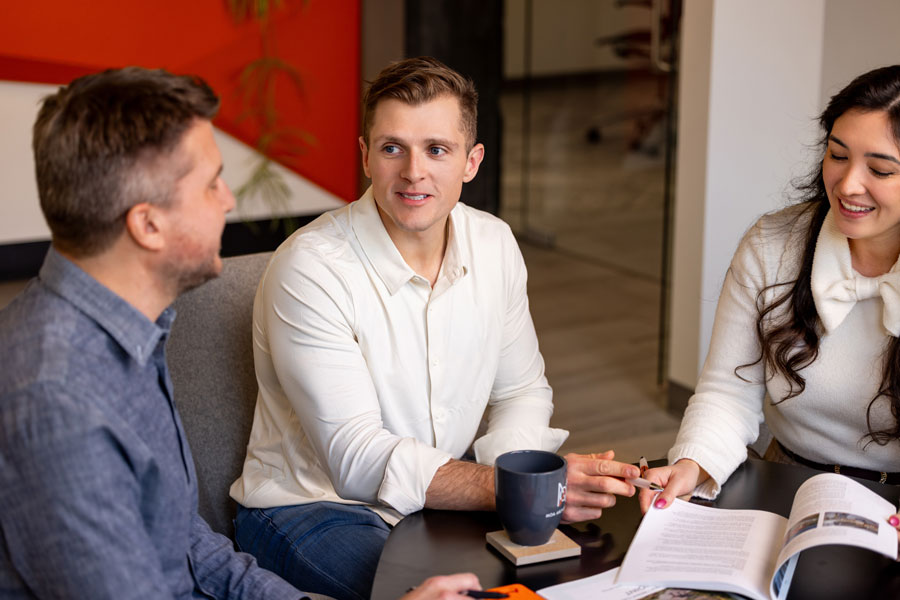 Three MOA Architecture team members engaged in an informal conversation around a coffee table, reflecting the firm's collaborative and open culture.