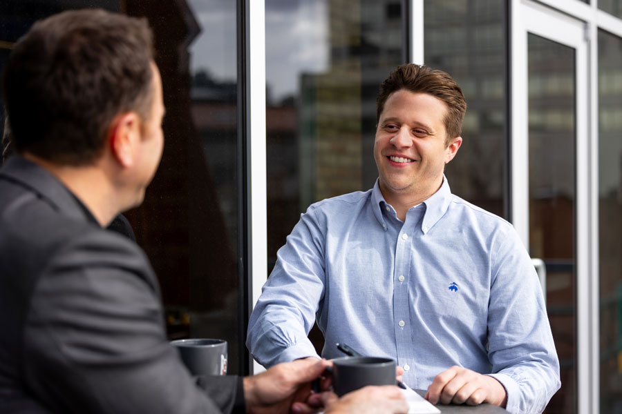 > `Two MOA Architecture colleagues sharing a relaxed conversation over coffee, illustrating the firm's culture of mentorship and mutual support.