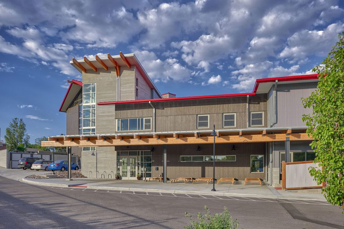 Exterior view of the Great Work Montessori PK-5 School building with a modern architectural design featuring large windows, a wooden canopy, and red roof accents under a partly cloudy sky.