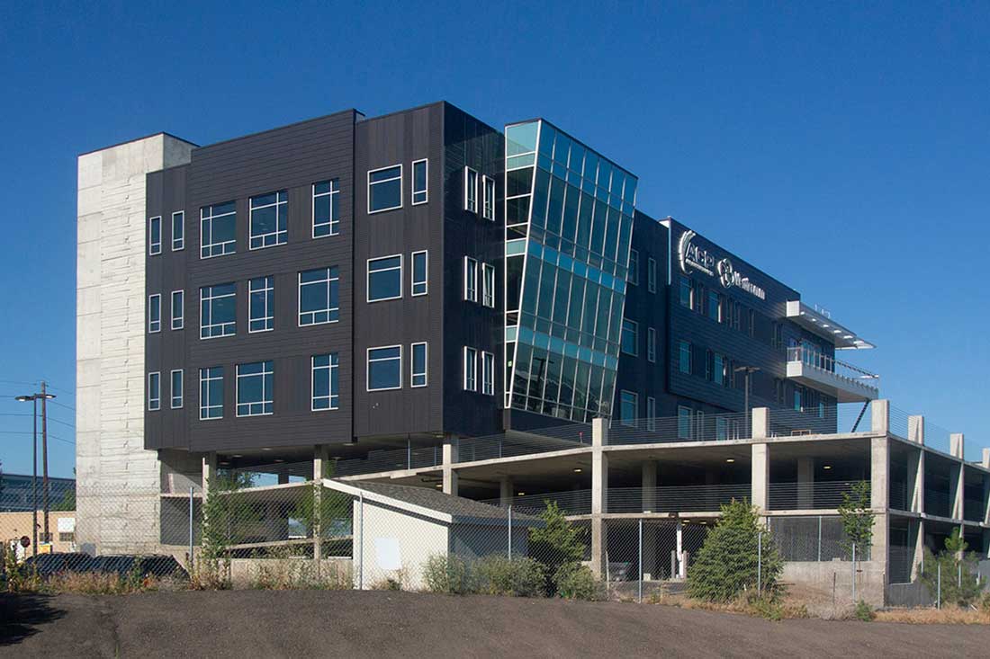 Modern multi-story office building with large glass windows and dark exterior panels under a clear blue sky.