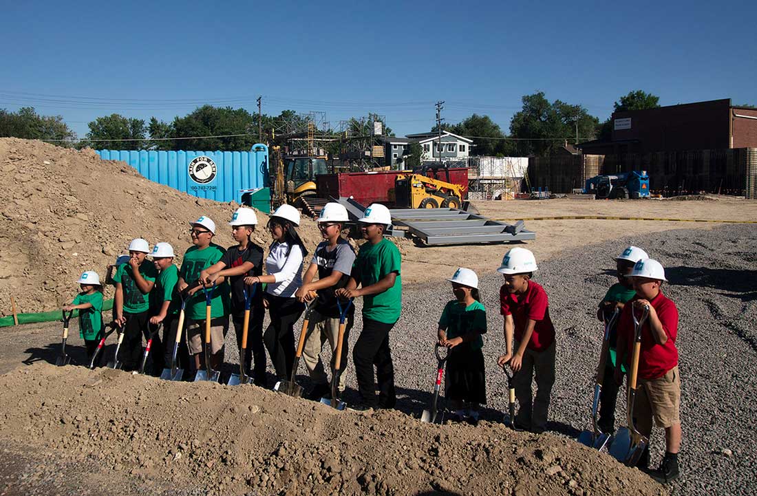 A group of young students shoveling dirt in a groundbreaking ceremony.