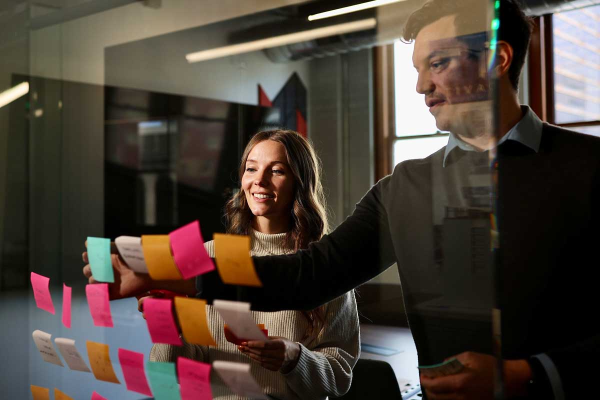 Two MOA Architecture team members arranging colorful sticky notes on a glass wall during a programming and conceptual design session with a client.