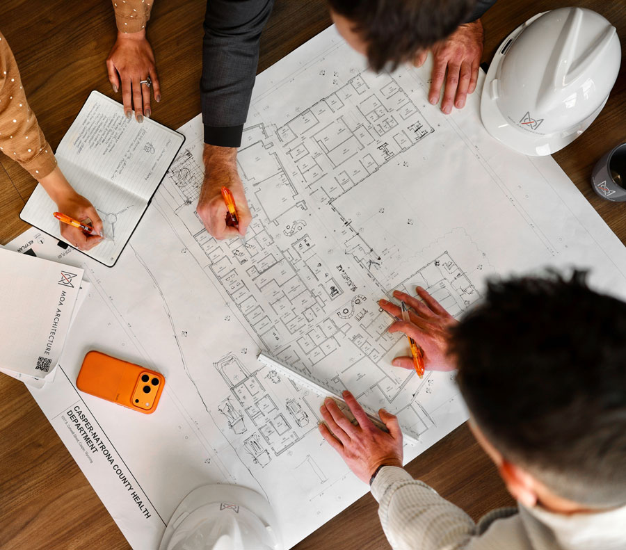 Overhead view of MOA Architecture team members reviewing construction drawings, with an MOA hard hat and project documents on the table.