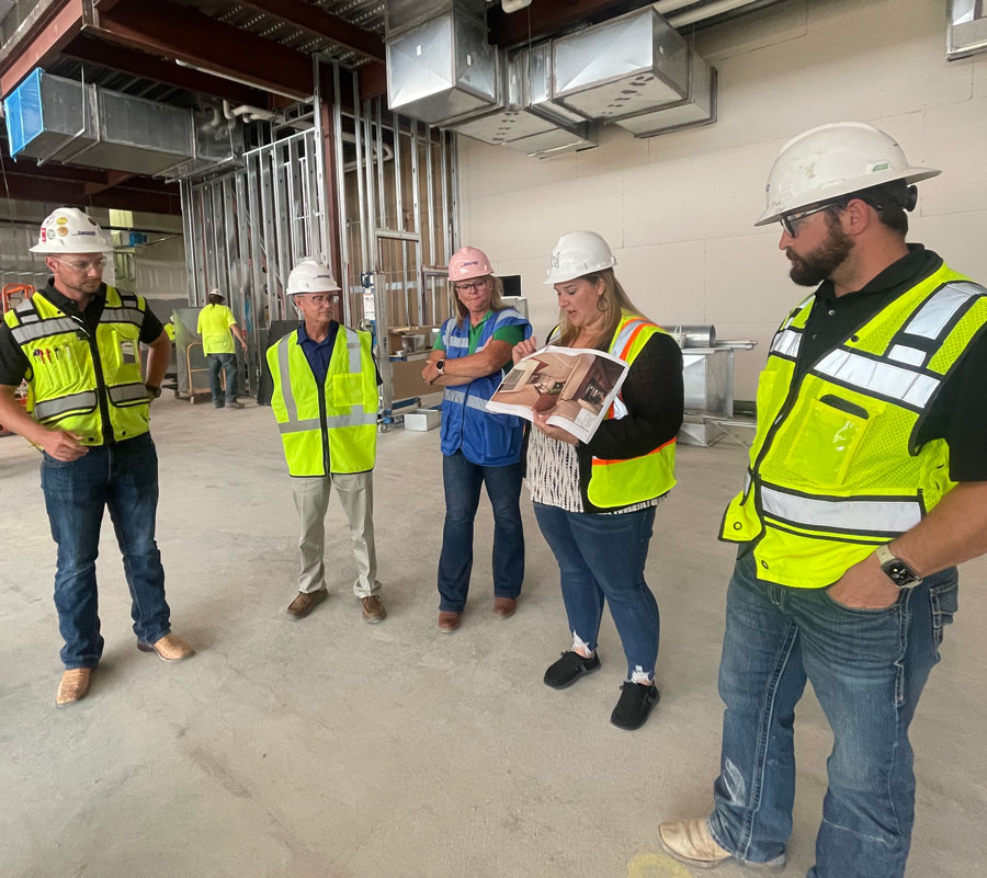 MOA team and contractors in hard hats reviewing design documents on an active construction site.
