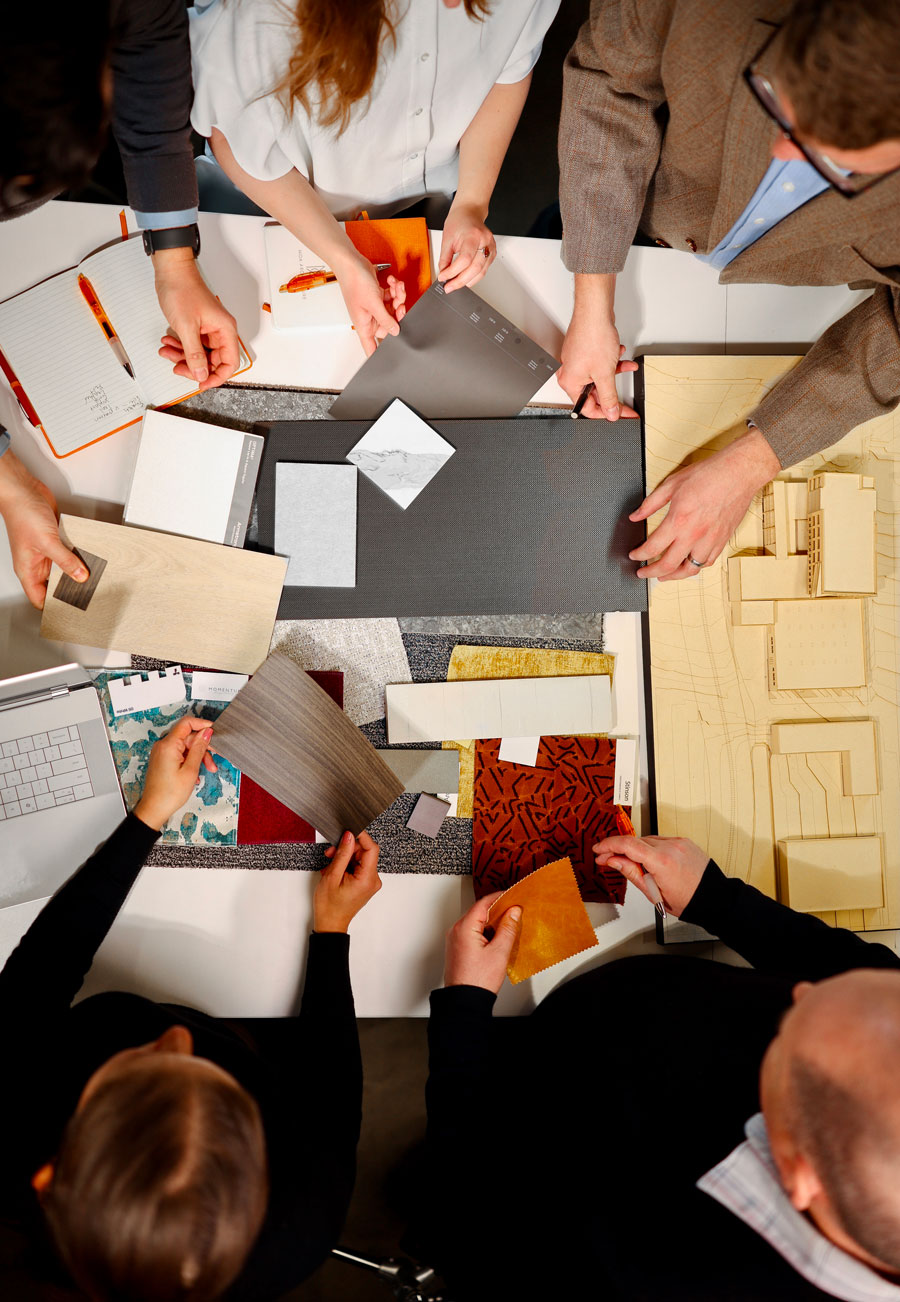 Overhead view of MOA team selecting fabric, tile, and finish samples alongside a physical building model.