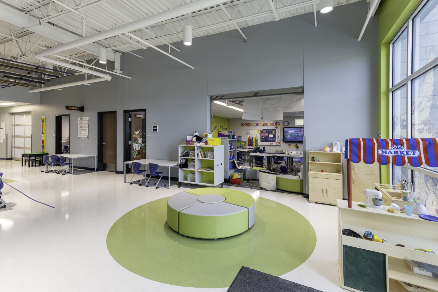 Central learning commons with a wide tiered stair, open circulation paths, mobile library shelving, soft seating areas, and suspended acoustic ceiling panels.