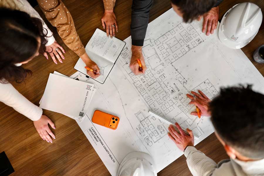 > `MOA Architecture team reviewing floor plans for the Casper-Natrona County Health Department project, gathered around a table with blueprints, hard hats, and markup pens.